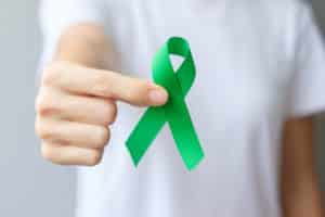 A woman holds a green ribbon for cerebral palsy awareness.